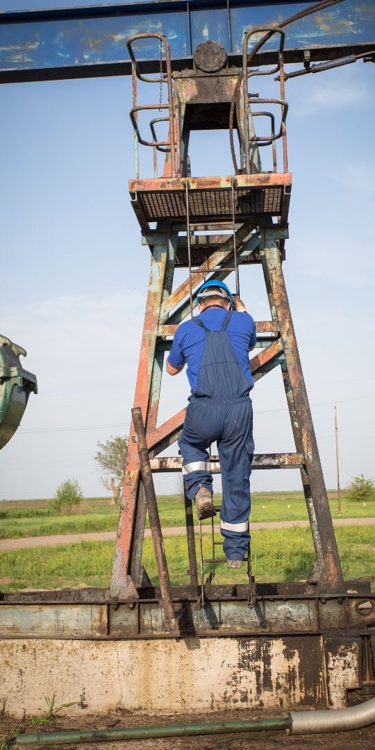 Field technician climbing a pumpjack for well servicing