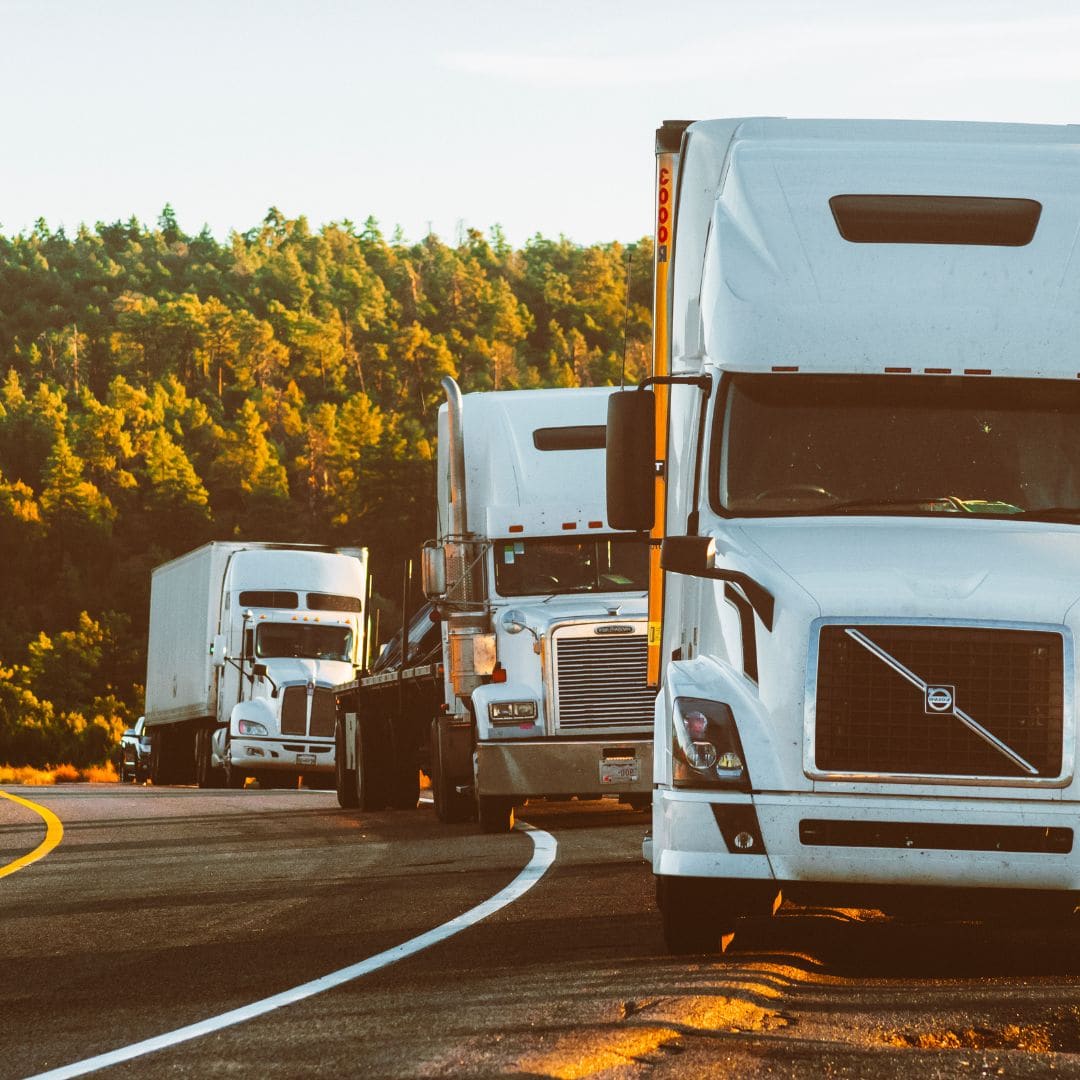 Small fleet of semi trucks in convoy on the highway