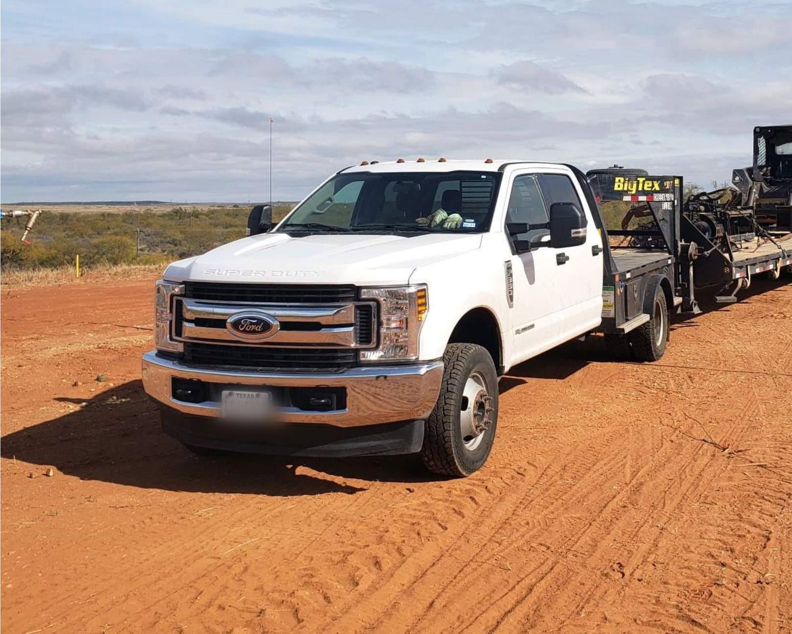 Hotshot dually pickup with gooseneck trailer loaded on an oilfield road